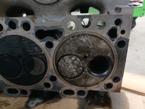 Diesel engine cylinder head showing severe combustion chamber damage after a dropped exhaust valve caused piston impact in an agricultural engine.
